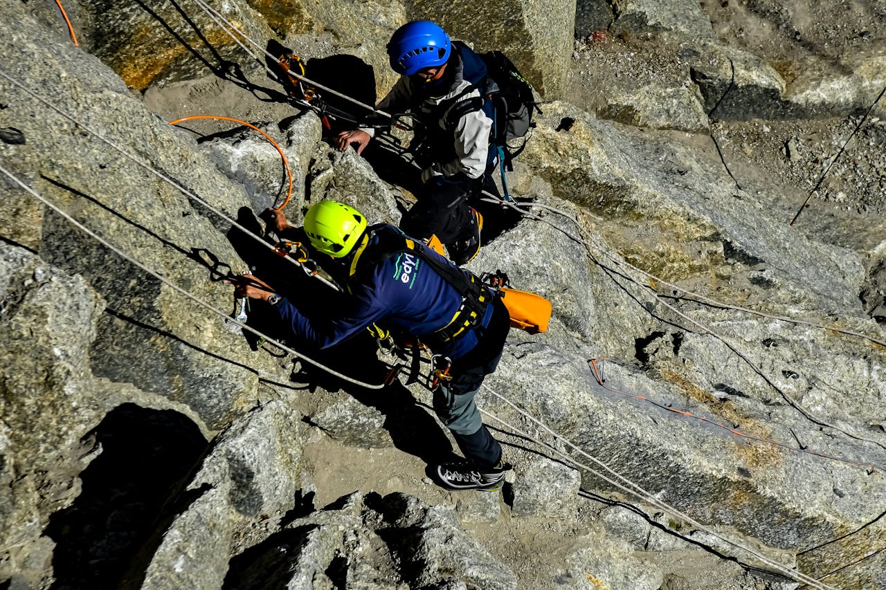 Two climbers scale a rocky mountain with ropes and safety gear, showcasing adventure and teamwork.