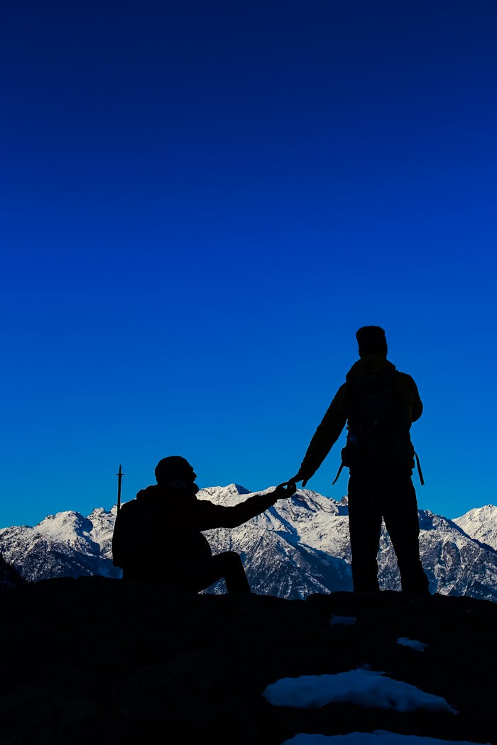 Silhouettes of hikers against snow-covered mountains and a vibrant blue sky.