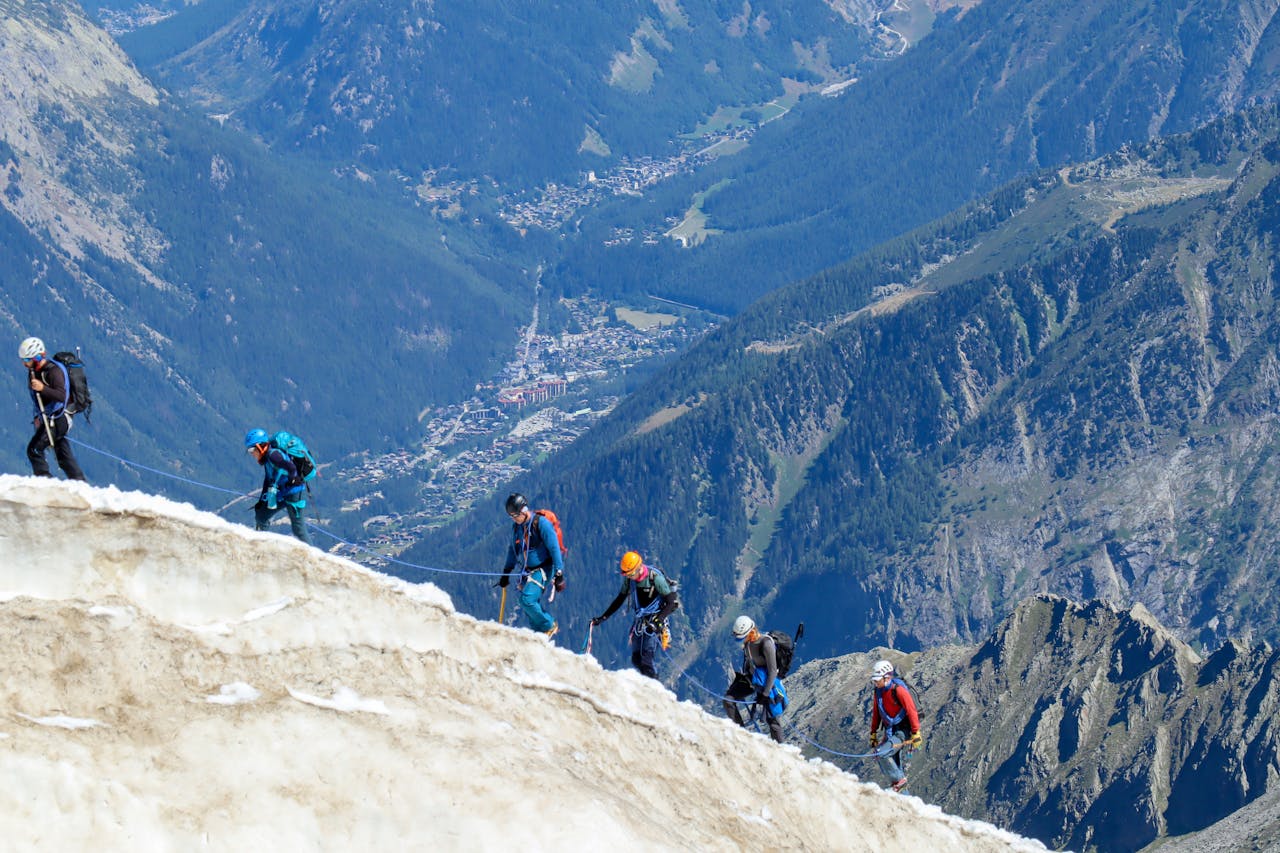 Adventurers climbing a snowy ridge with stunning views of Chamonix in the background.