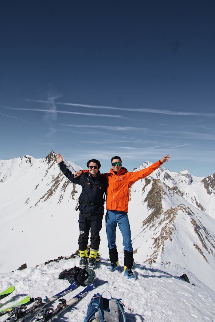 Two skiers celebrate on a snowy mountain peak under clear blue skies. Perfect adventure moment captured.