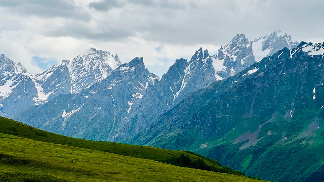 Scenic landscape of the snowy Caucasus Mountains under a cloudy sky with lush green foreground.
