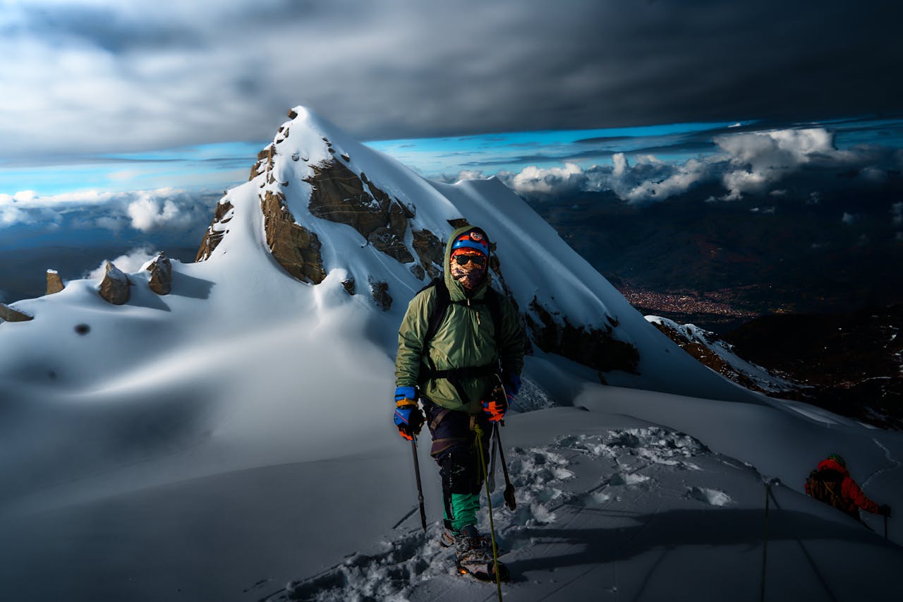 Climber on icy Andean peak near Huaraz, Peru, against dramatic sky.
