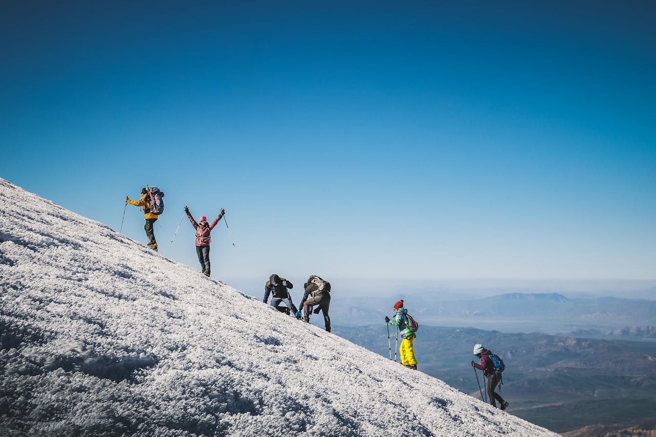 Adventurous group climbing a snowy mountain under clear blue skies, showcasing determination and teamwork.